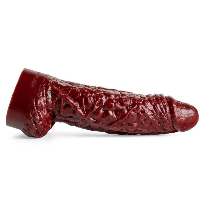 The Theeng dildo lying on its side, showcasing its rugged, rocky textures and pulled-back foreskin detail in blood red silicone.