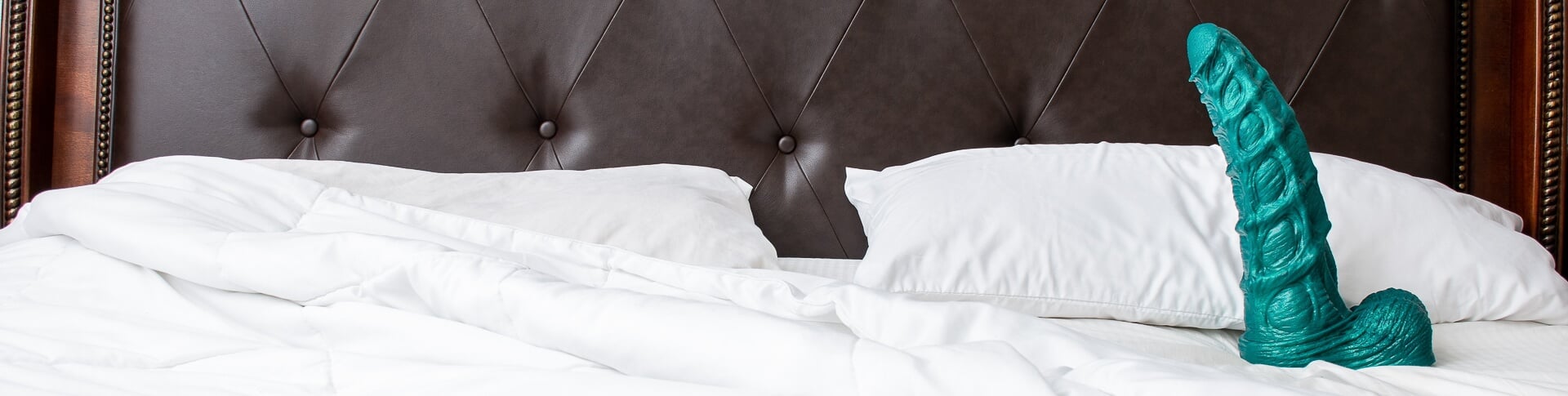 Teal hand-poured, platinum-cured silicone adult toy on white bedding in a bedroom&mdash;Mr. Hankey&rsquo;s Toys, USA-made craftsmanship.