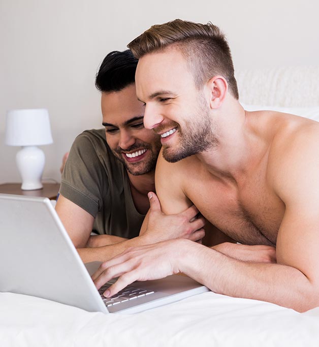 2 People laying down on a bed smiling while looking at a latop.